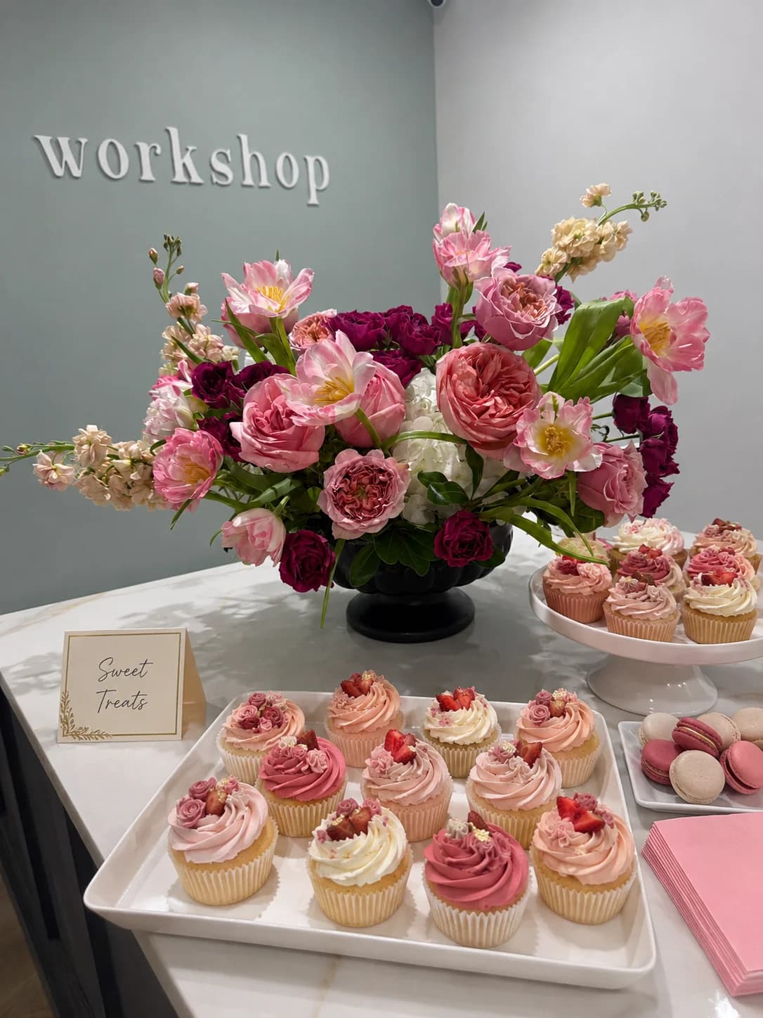Dessert table with pink cupcakes, macarons and a large pink floral arrangement
