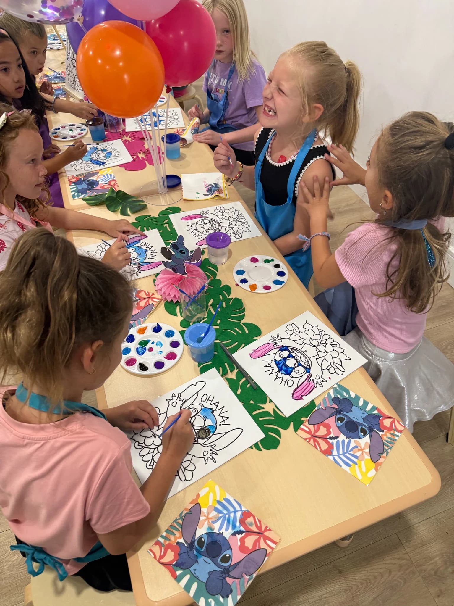 Girls in aprons painting canvas boards at a birthday party with tropical table decorations