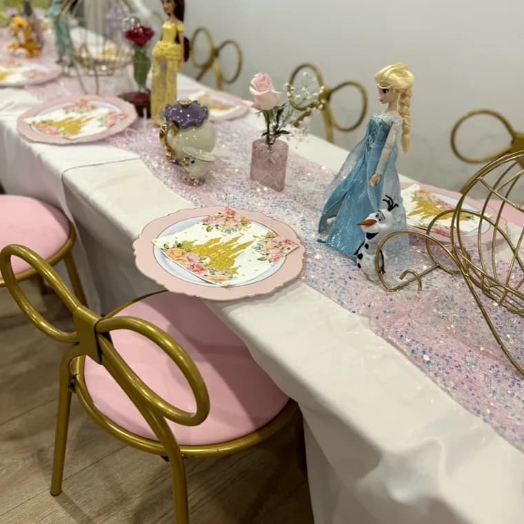 Princess-themed party table with pink chairs, floral plates and a sparkly runner