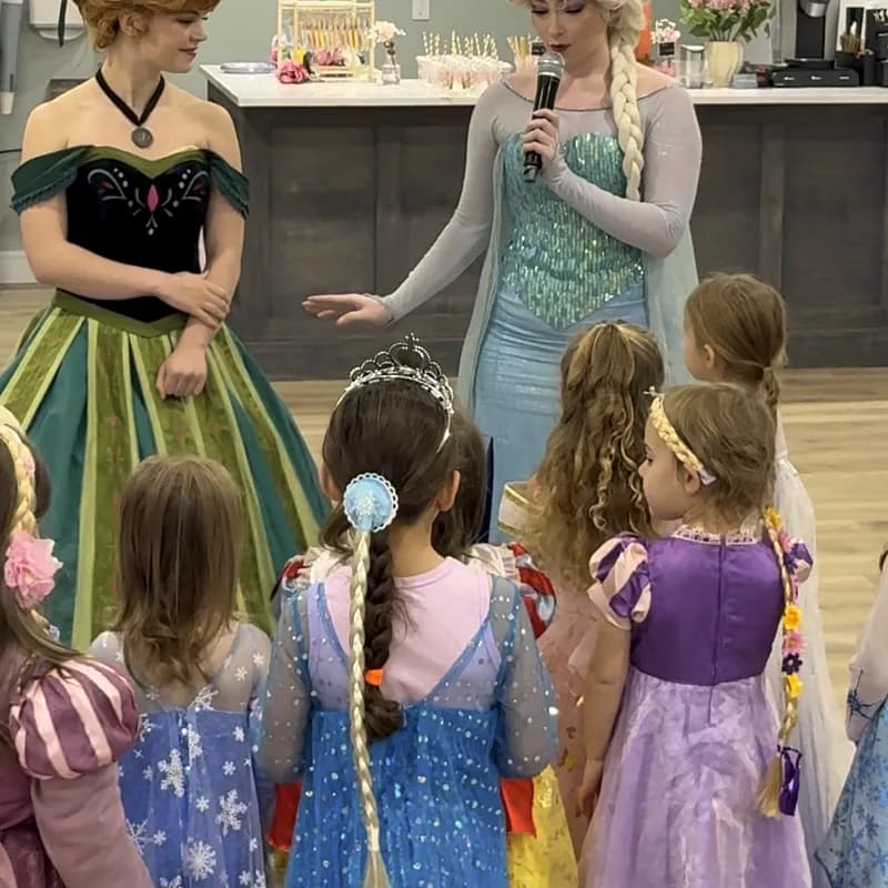 Kids in princess dresses gathered around two costumed princesses at a birthday party